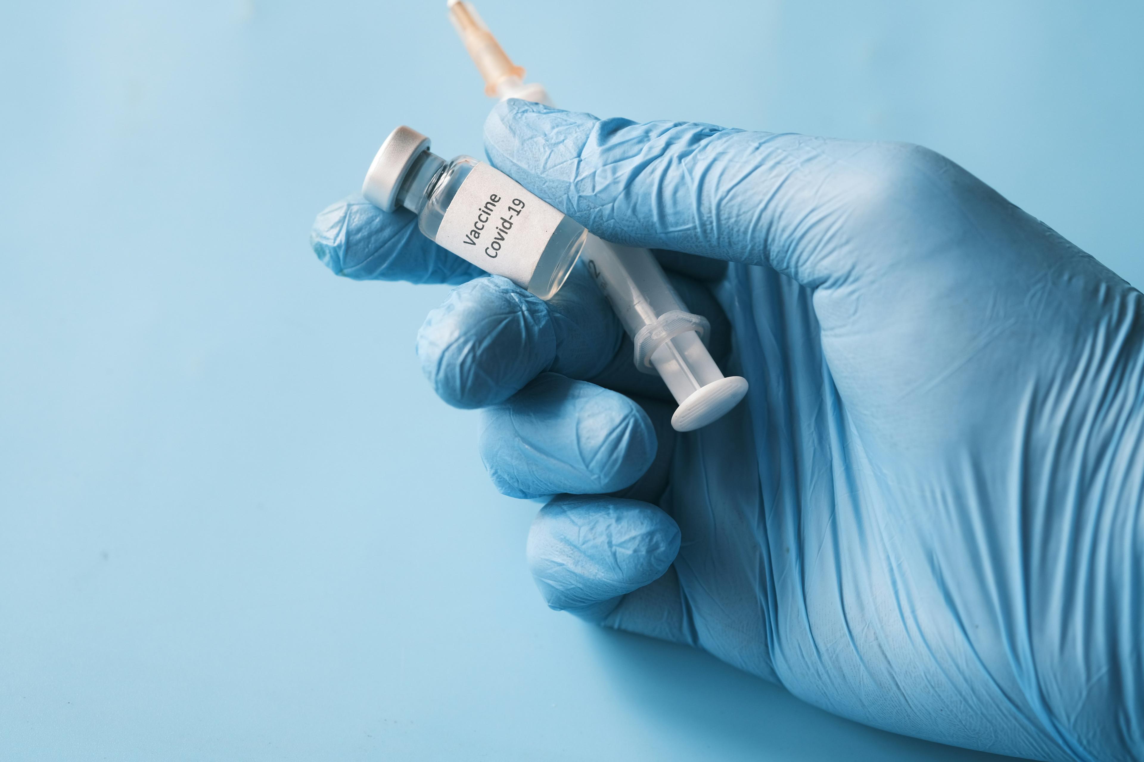 Gloved hand holding a vaccine vial and syringe