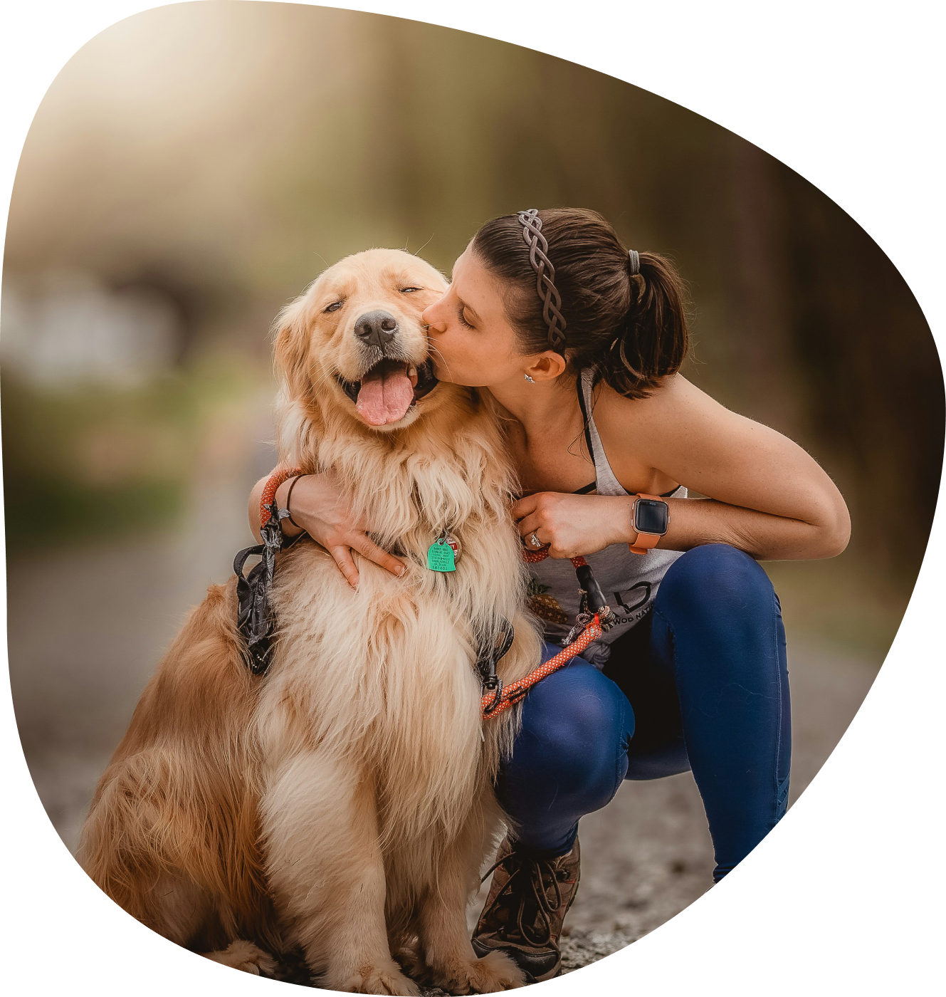 Woman crouching to kiss her golden retriever on a woodland path