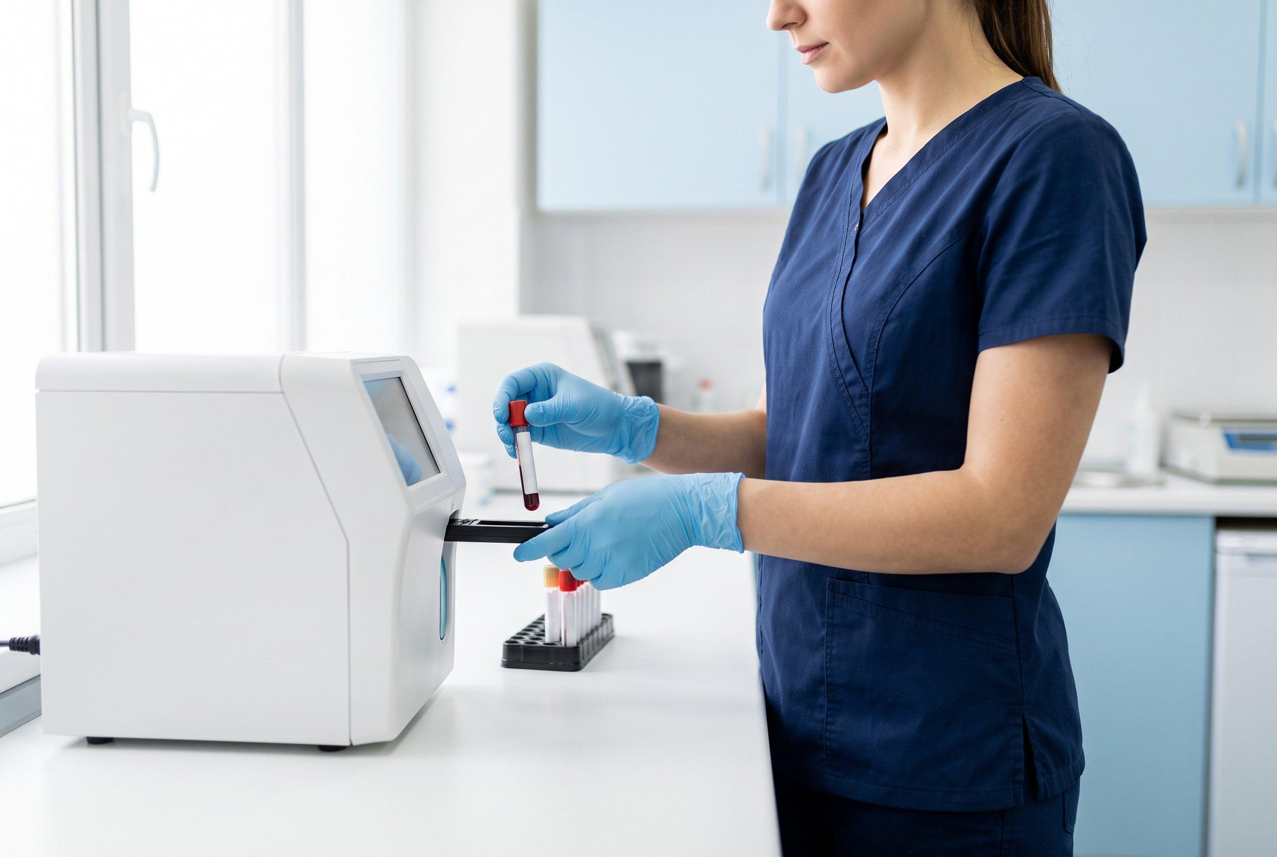 Vet nurse in gloves loading a blood sample tube into a benchtop analyser